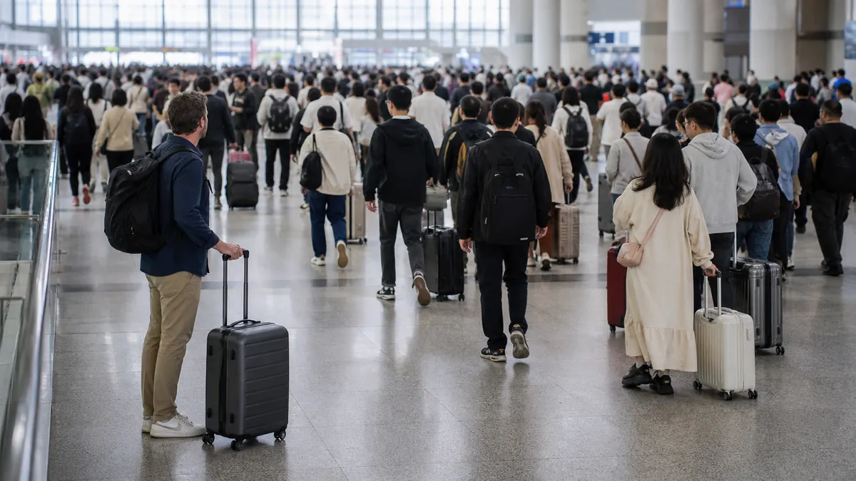 Traveler waiting with compact luggage beside a busy China rail station passenger flow